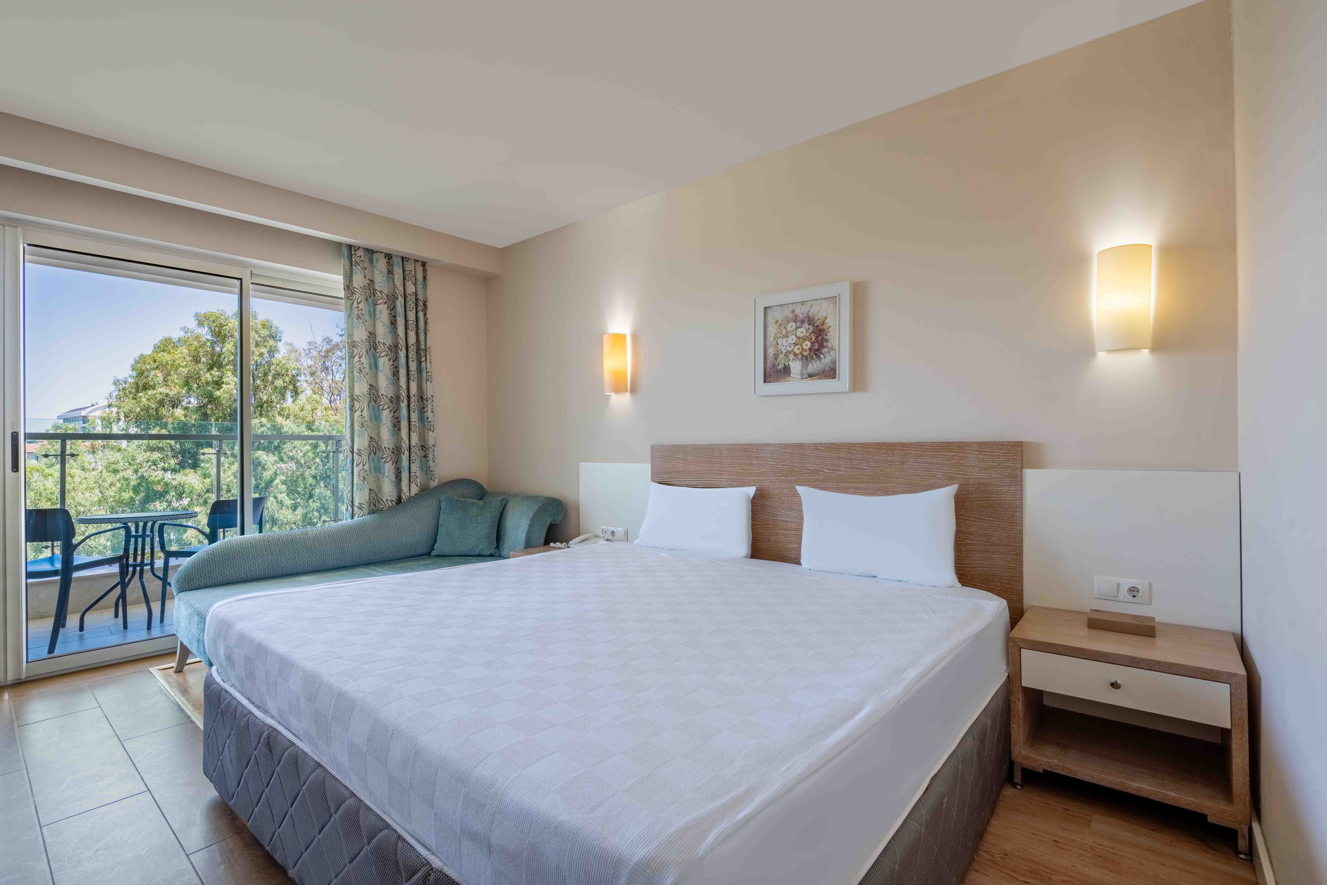 A guest room with a double bed, sofa and balcony overlooking trees.
